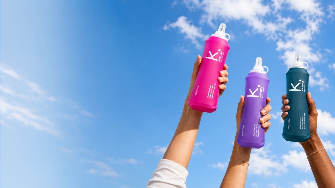 Three hands raising Khydra soft flasks against a blue sky